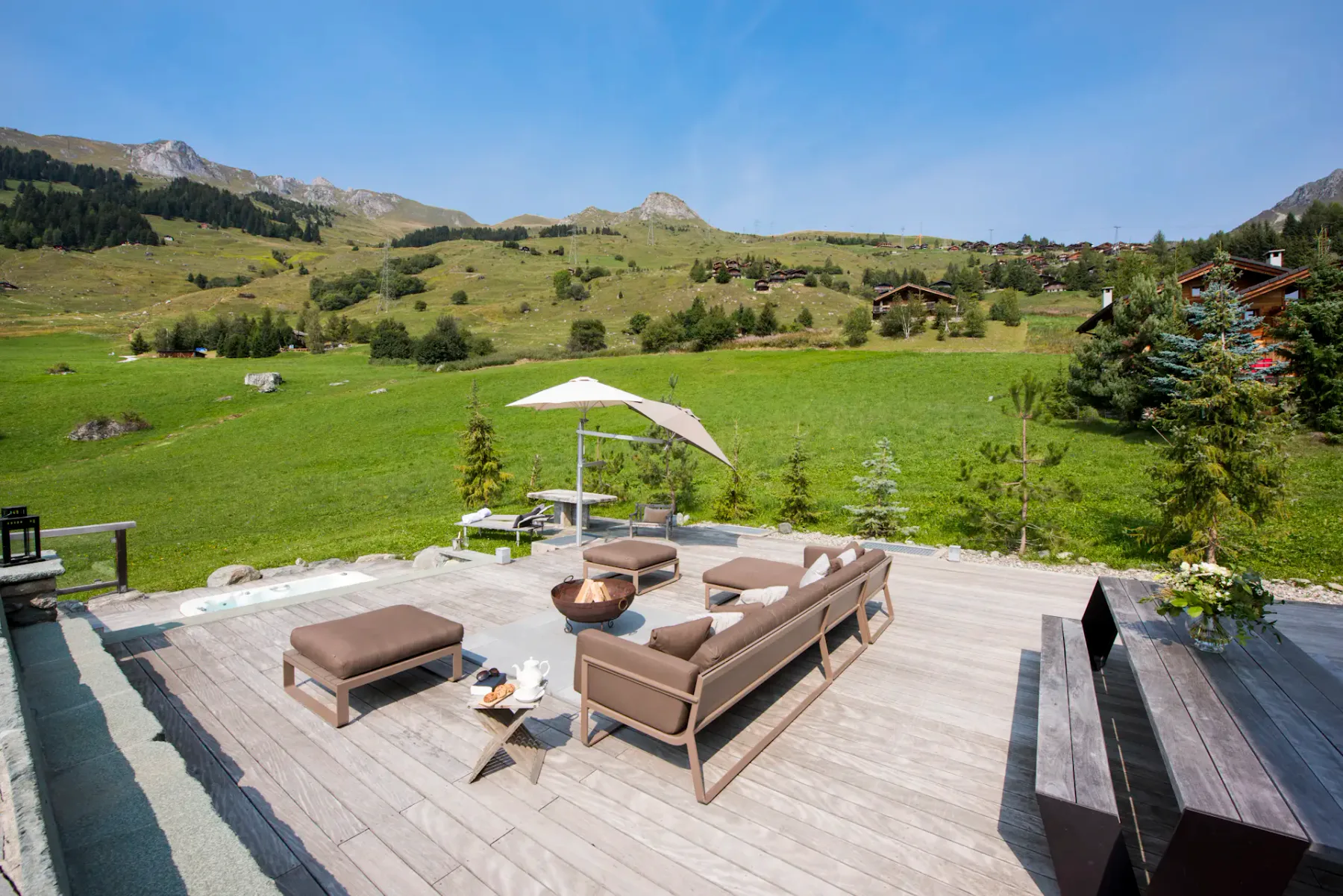 Bañera de hidromasaje al aire libre en una terraza de madera con montañas visibles al fondo.