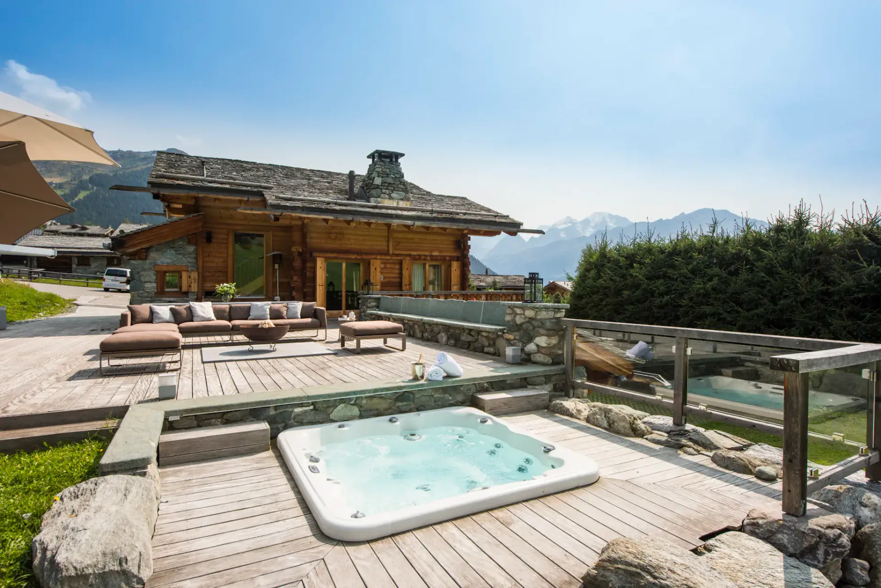 Bañera de hidromasaje al aire libre en una terraza de madera con montañas visibles al fondo.