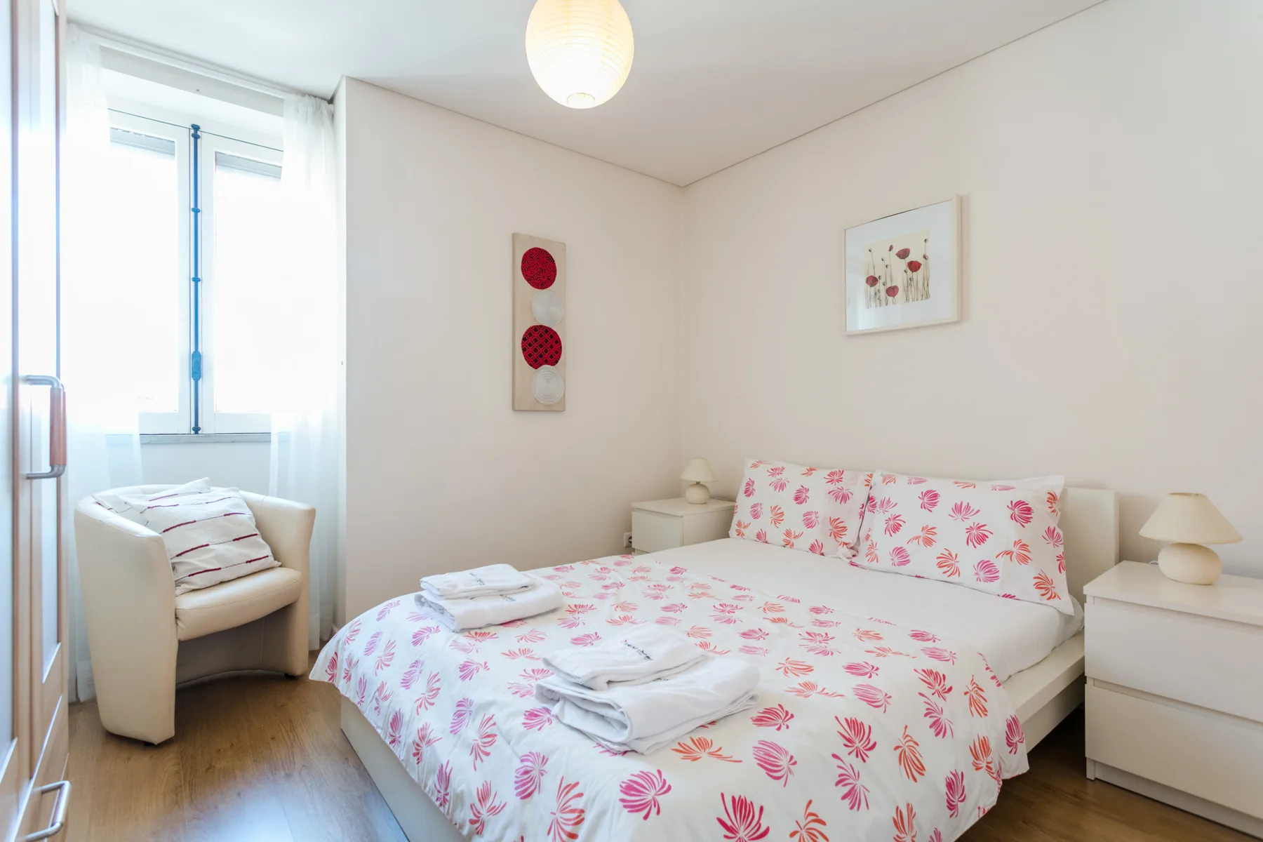 Dormitorio con una cama cubierta de ropa de cama floral rosa y una ventana.