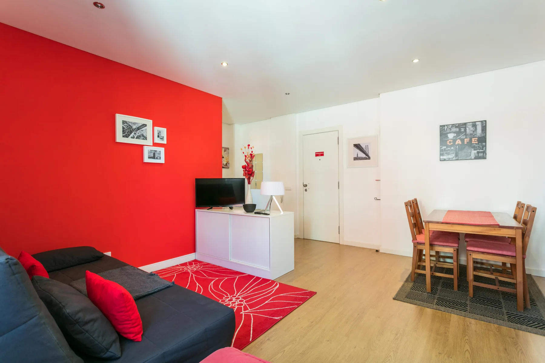 Una luminosa sala de estar y comedor con asientos oscuros, una alfombra roja y una mesa de comedor de madera.