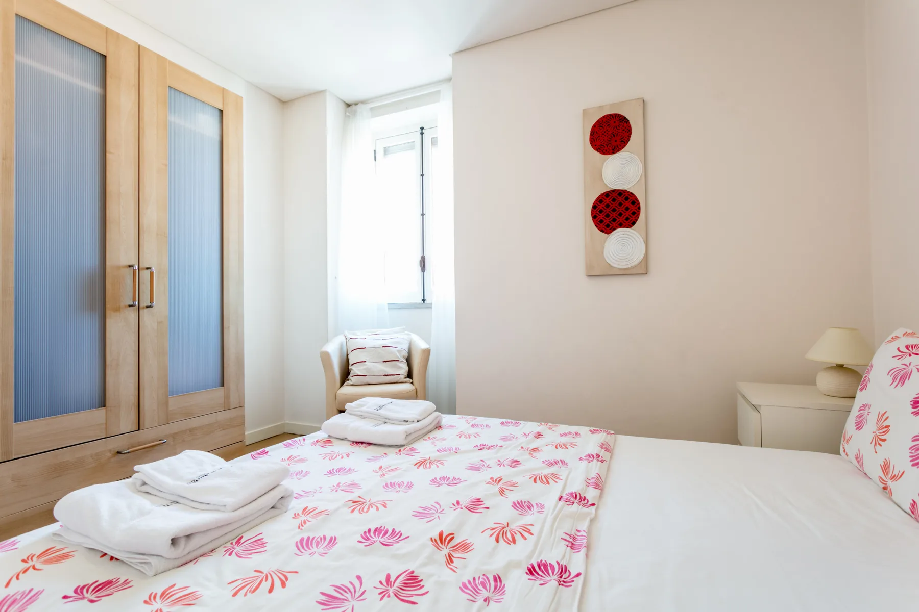 Un dormitorio con una colcha floral, toallas dobladas y un armario.