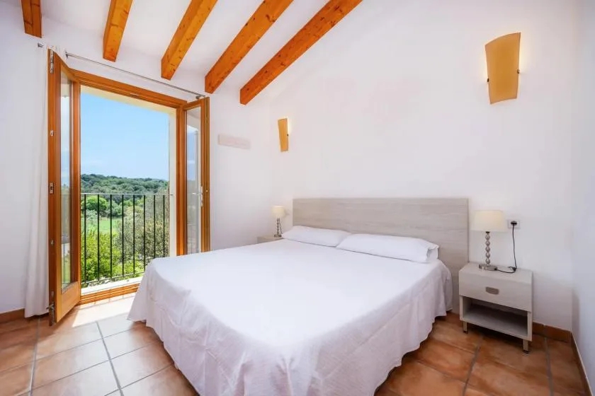 A bright bedroom with a white bed and open doors overlooking greenery.