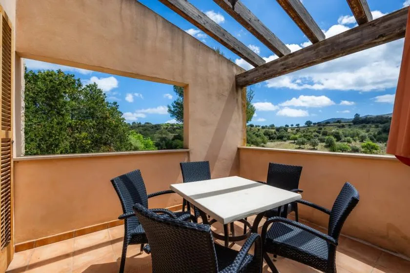 A sunny outdoor dining area with a table and seating overlooking green hills.