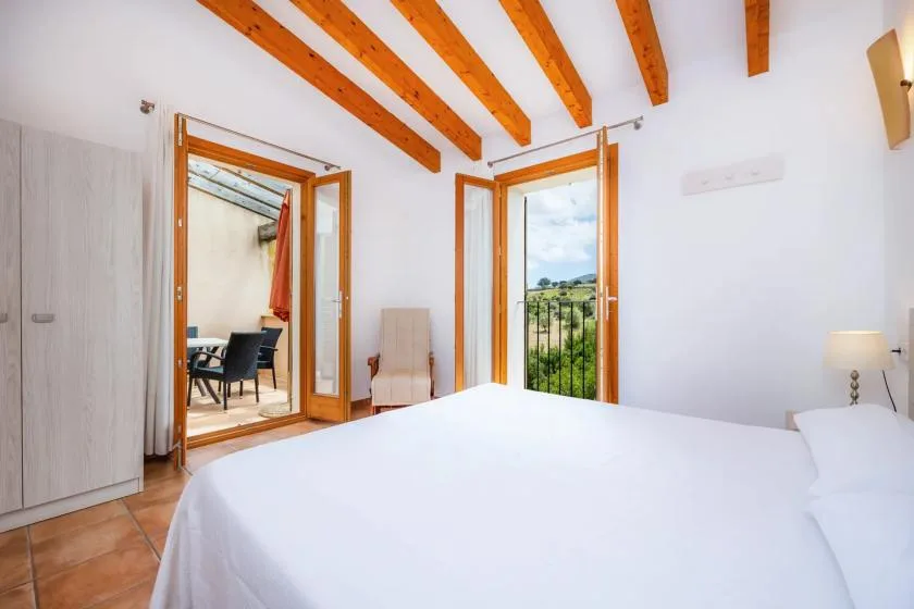 A bright bedroom with a white bed and open wooden doors to a balcony.