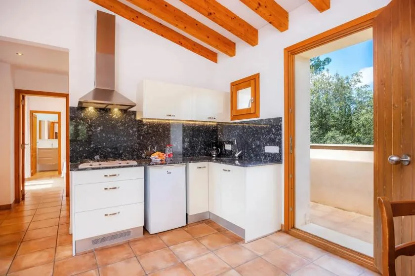A bright kitchen with white cabinetry, dark countertops, and exposed wooden ceiling beams.