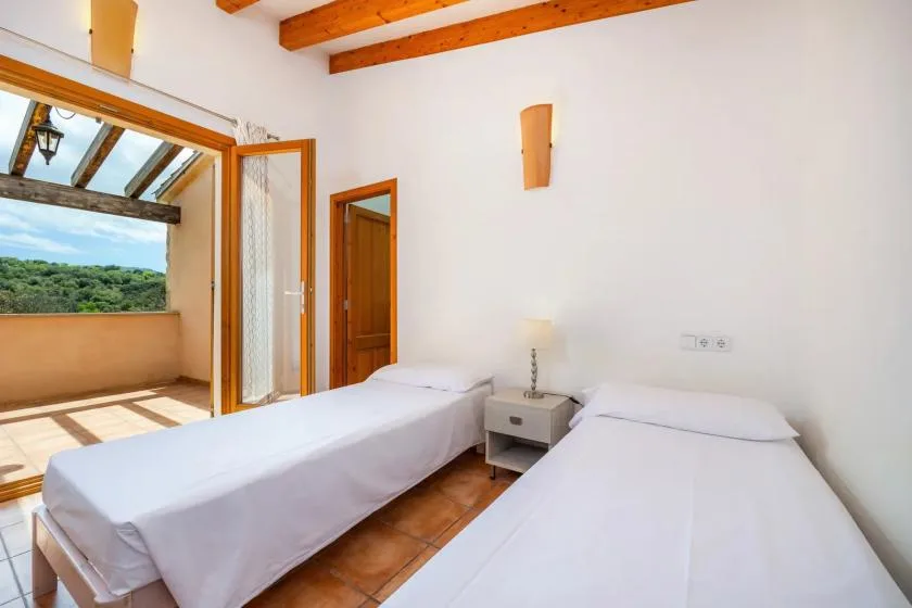 A bright bedroom with two beds and an open doorway to a terrace.