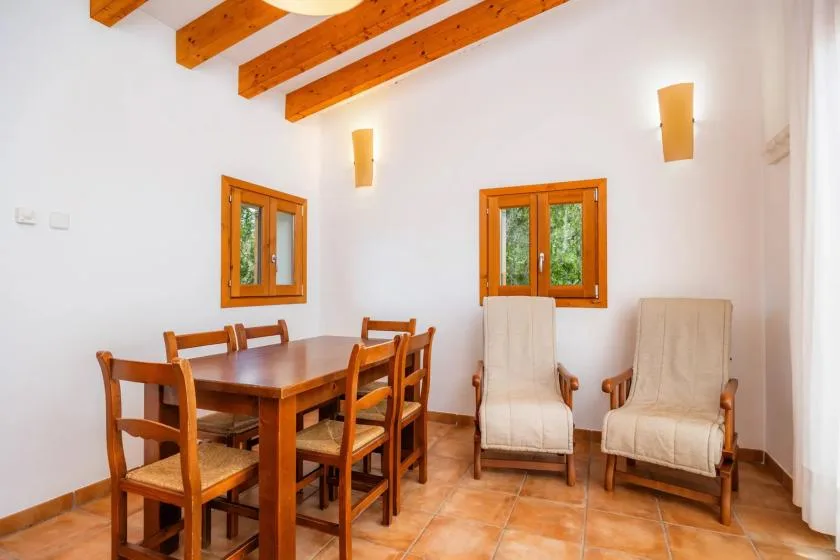A dining area with a wooden table and chairs beside two windows.