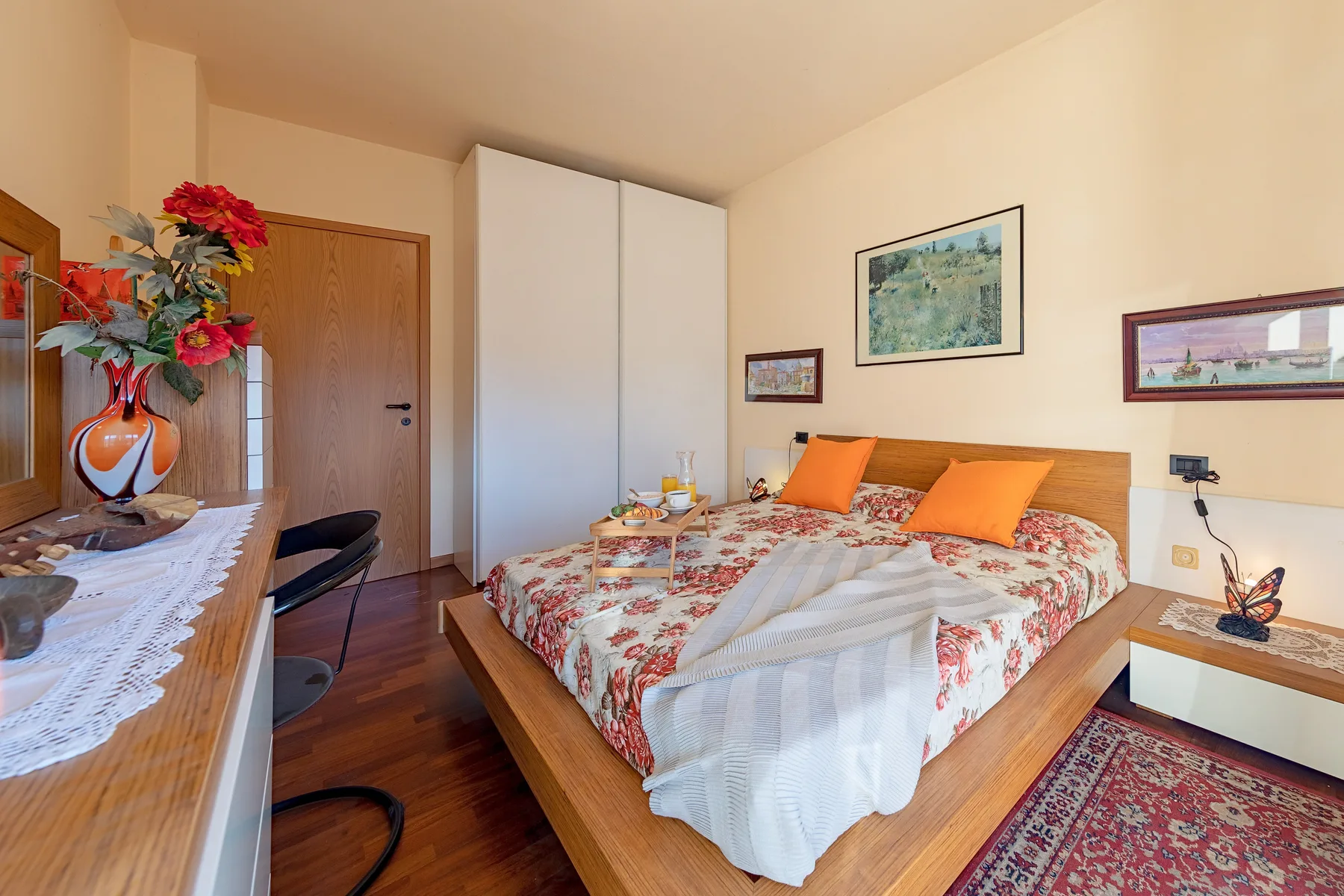 Un dormitorio con una cama de madera, ropa de cama floral y un pequeño escritorio al lado.