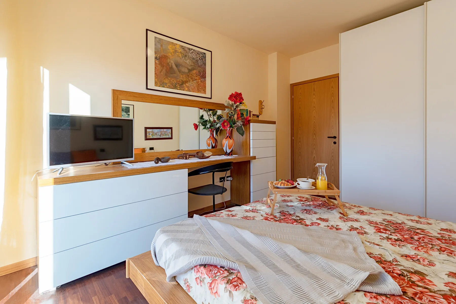 Un dormitorio con ropa de cama floral, un escritorio y un televisor.