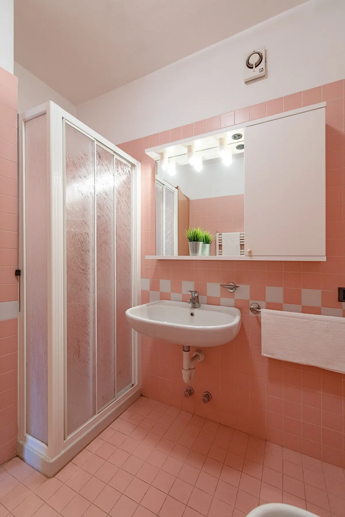 Un baño con azulejos rosas, ducha, lavabo y espejo grande.