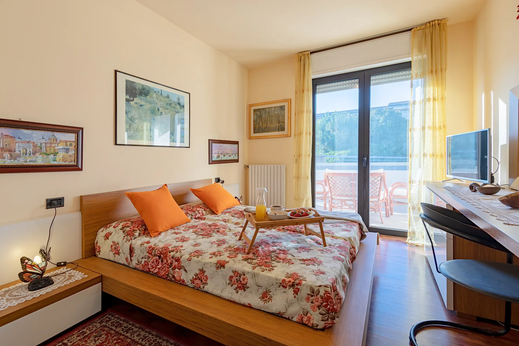 Un dormitorio con una colcha floral, una mesita de noche y puertas de vidrio que dan a un balcón.