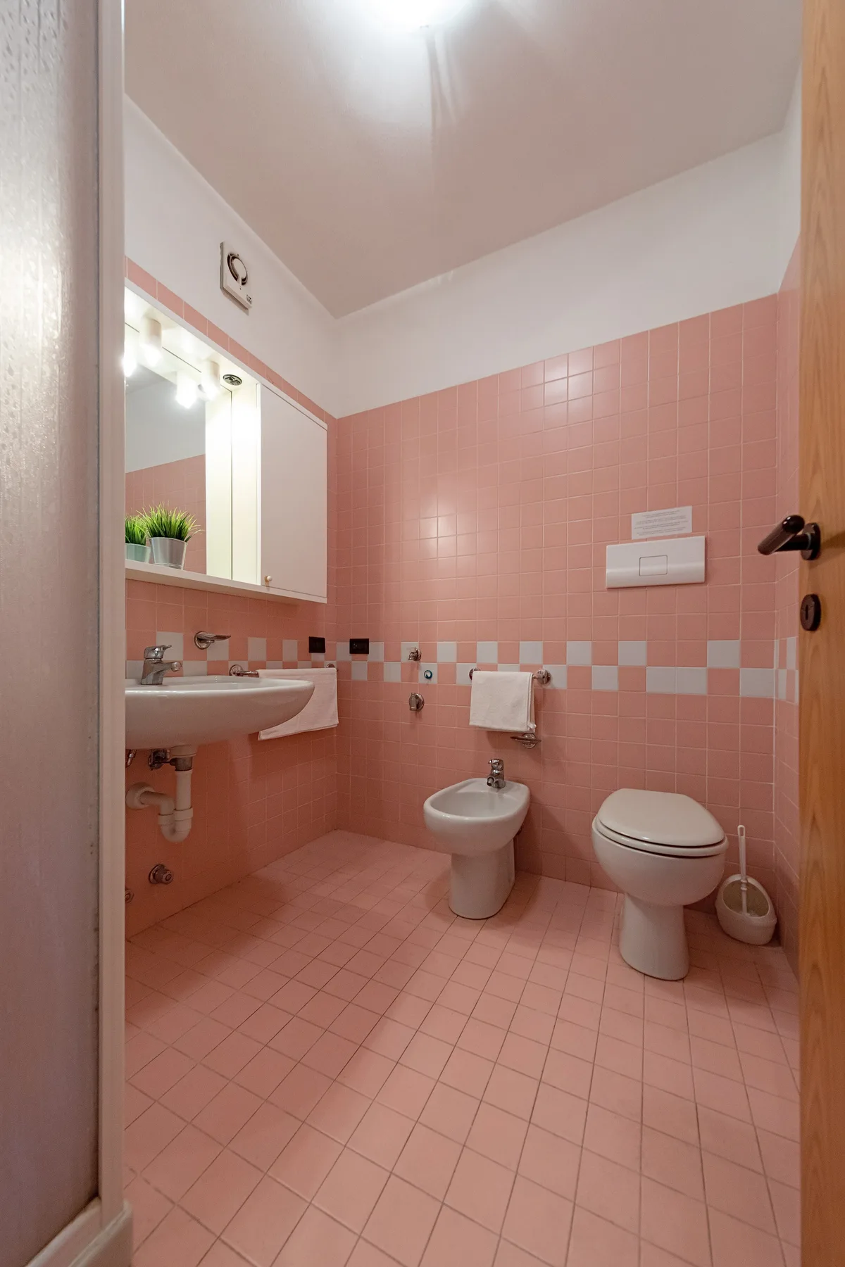 Un baño con azulejos rosas, lavabo, bidé e inodoro.