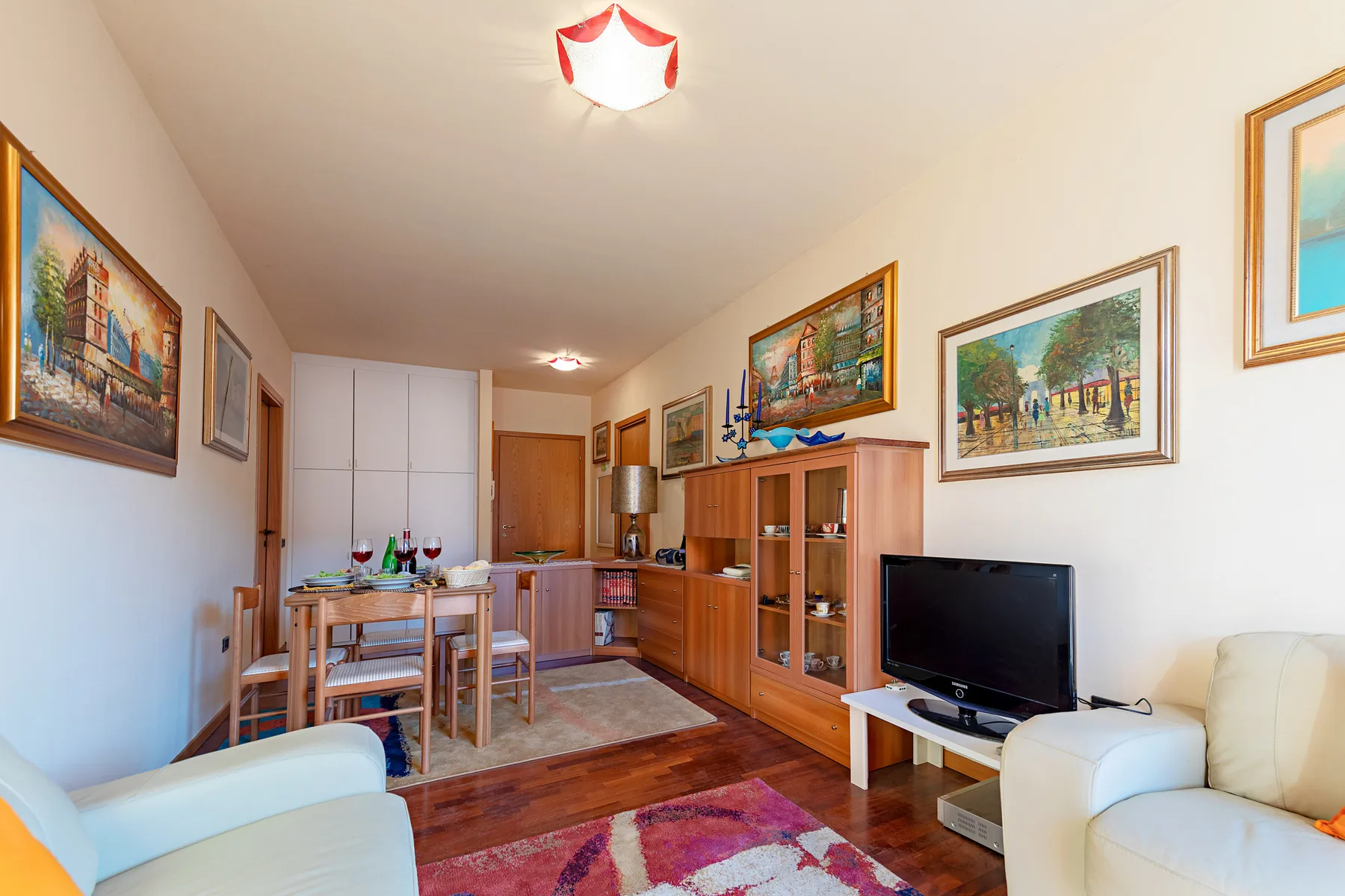 Una zona de estar y comedor con muebles de madera, un televisor y cuadros enmarcados.
