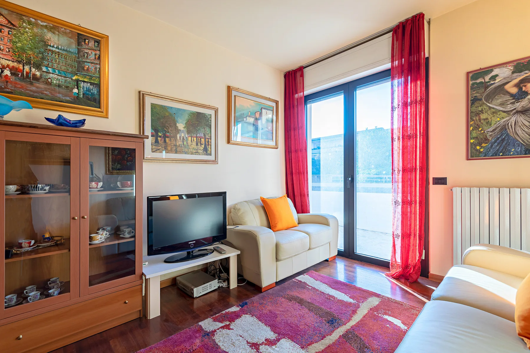 Una sala luminosa con asientos, un televisor y cortinas rojas junto a las puertas de vidrio.