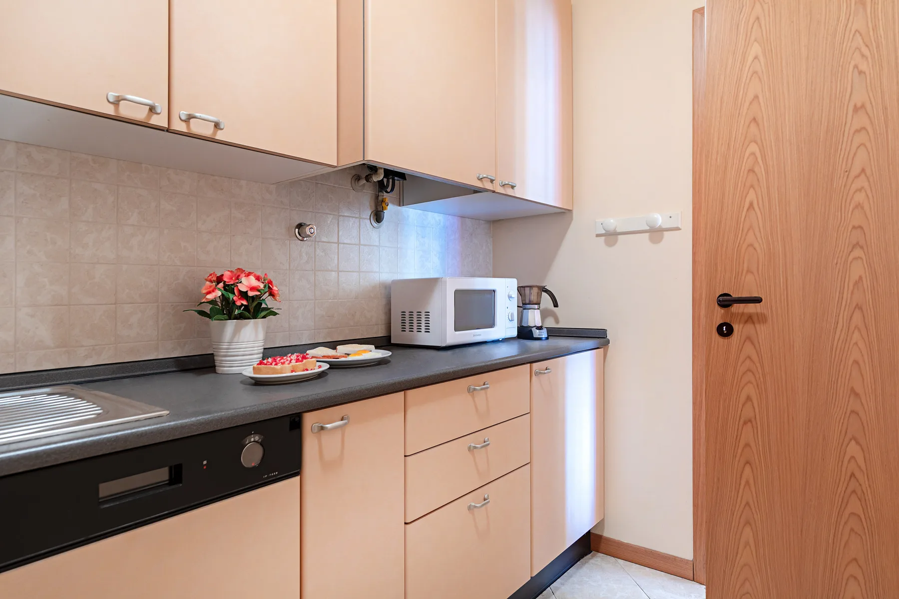 Una cocina compacta con gabinetes claros, una encimera oscura y un microondas.