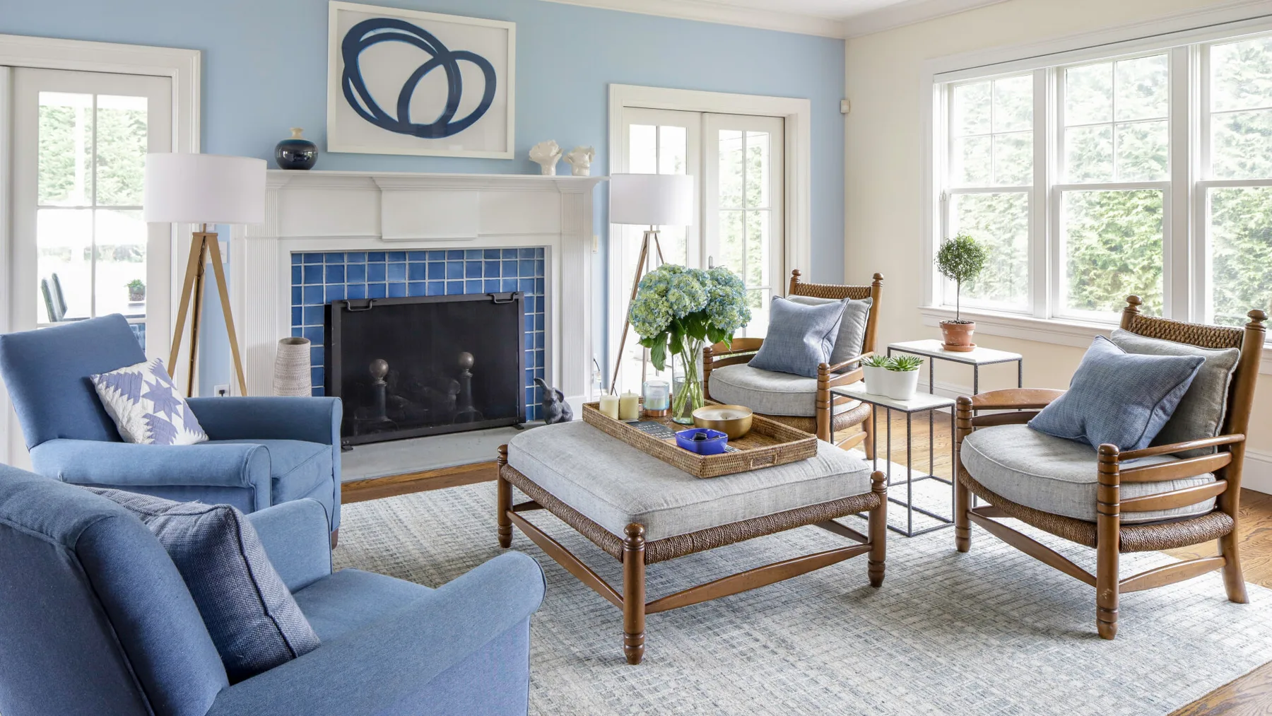 A bright living room with blue seating arranged around a fireplace and coffee table.