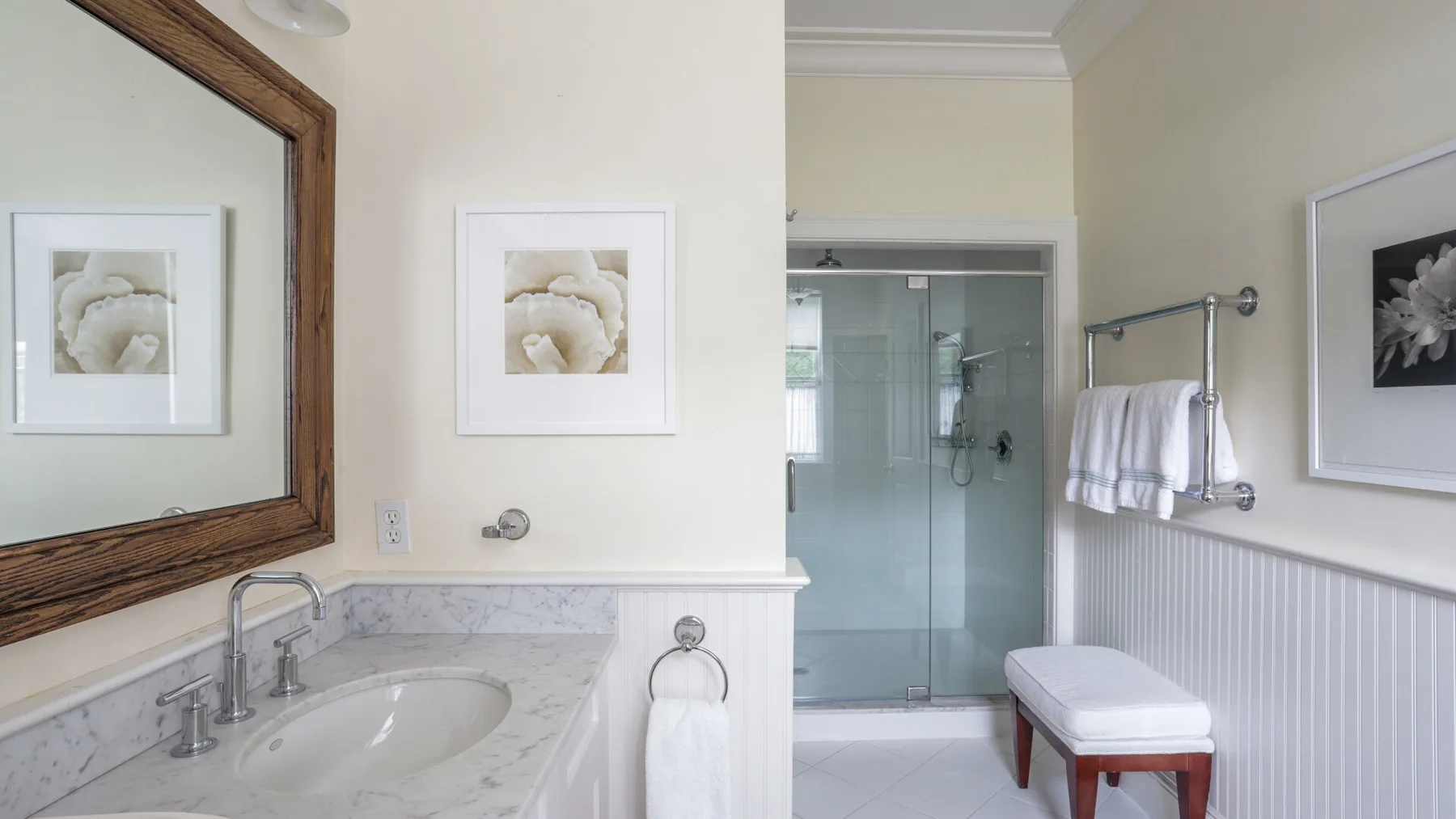 A bright bathroom with a glass shower, sink, and framed floral artwork.