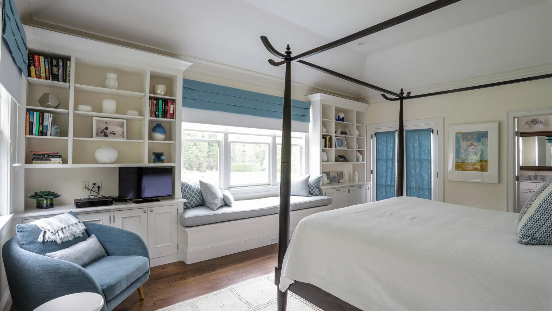 A bright bedroom with a large bed, built-in shelves, and a window seat.