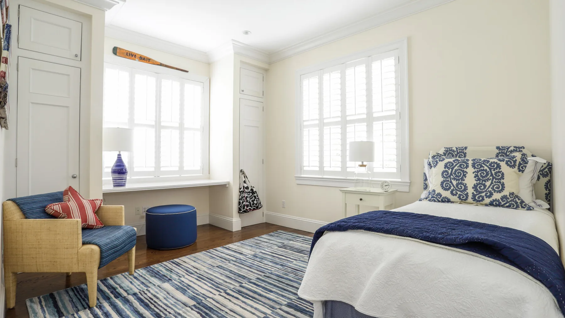 A bright bedroom with a bed, seating, and large shuttered windows.