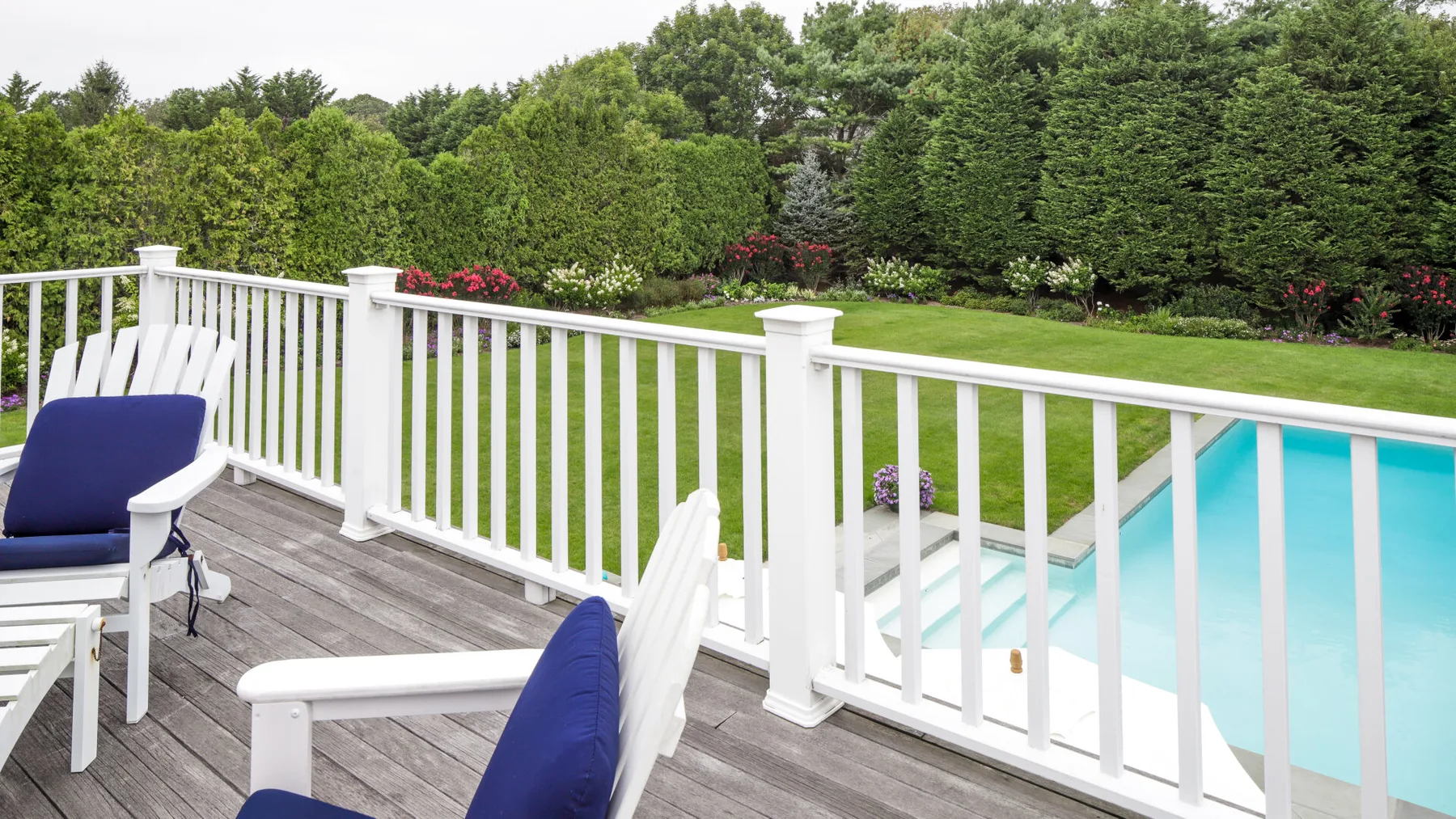 A wooden deck overlooks a swimming pool, with white seating beside the railing.