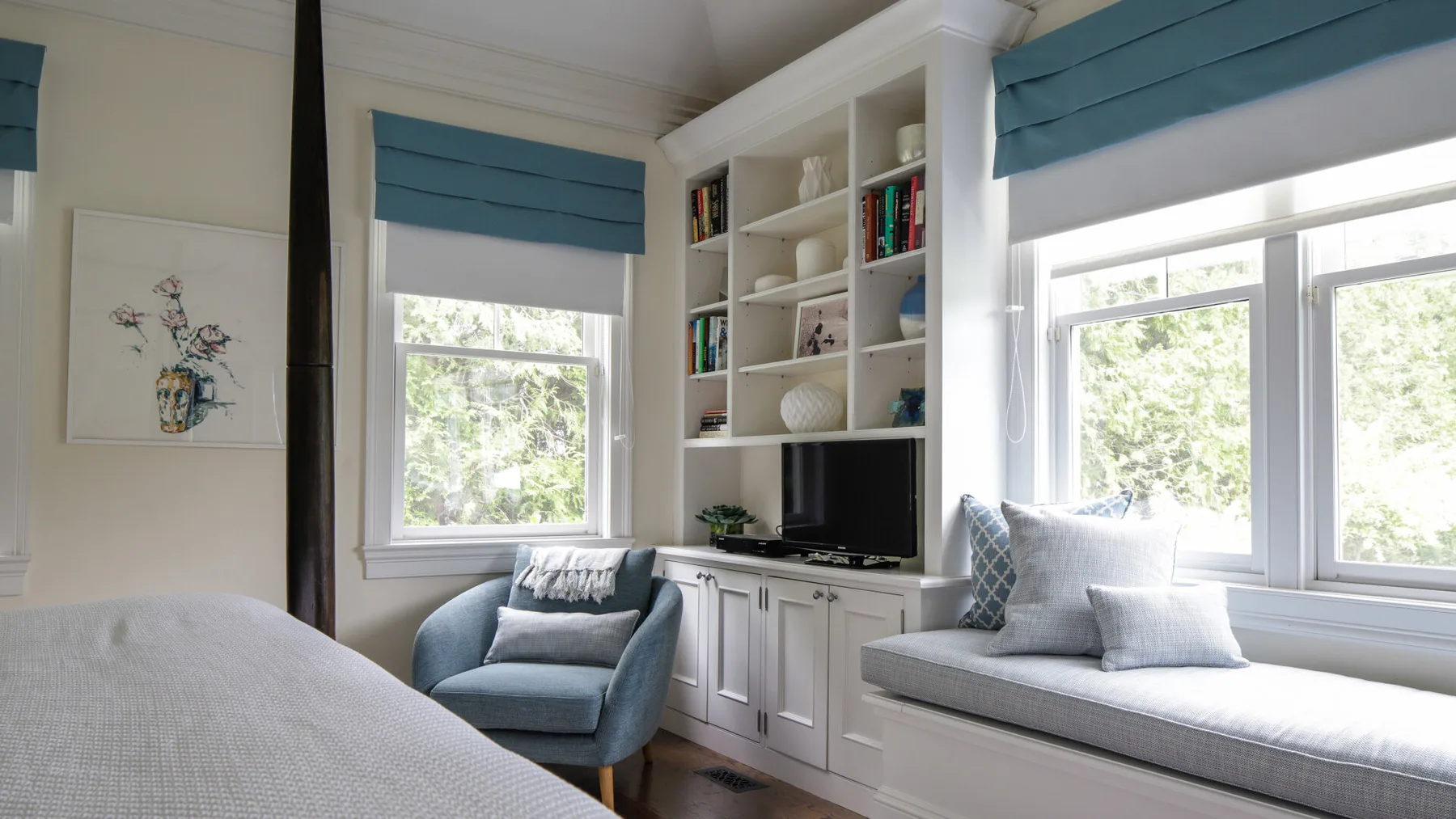 A bright bedroom has a bed beside a window seat and built-in shelves.