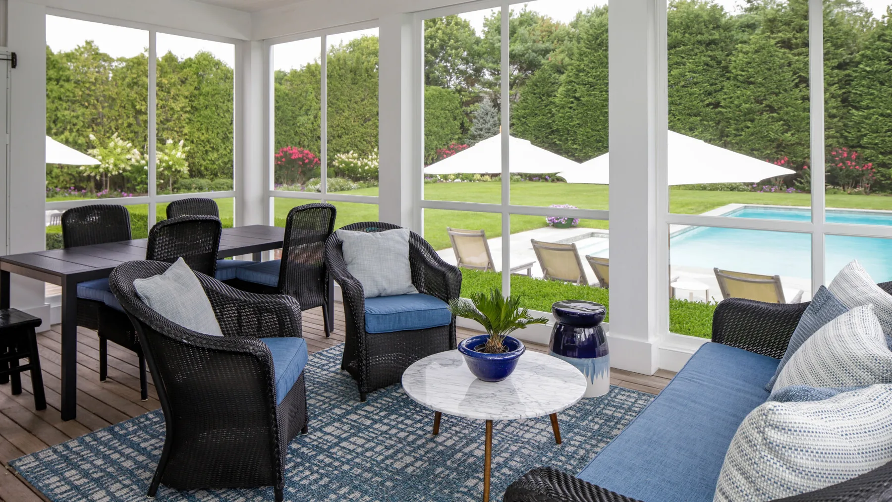A bright screened-in patio with seating, a dining table, and views of a swimming pool.
