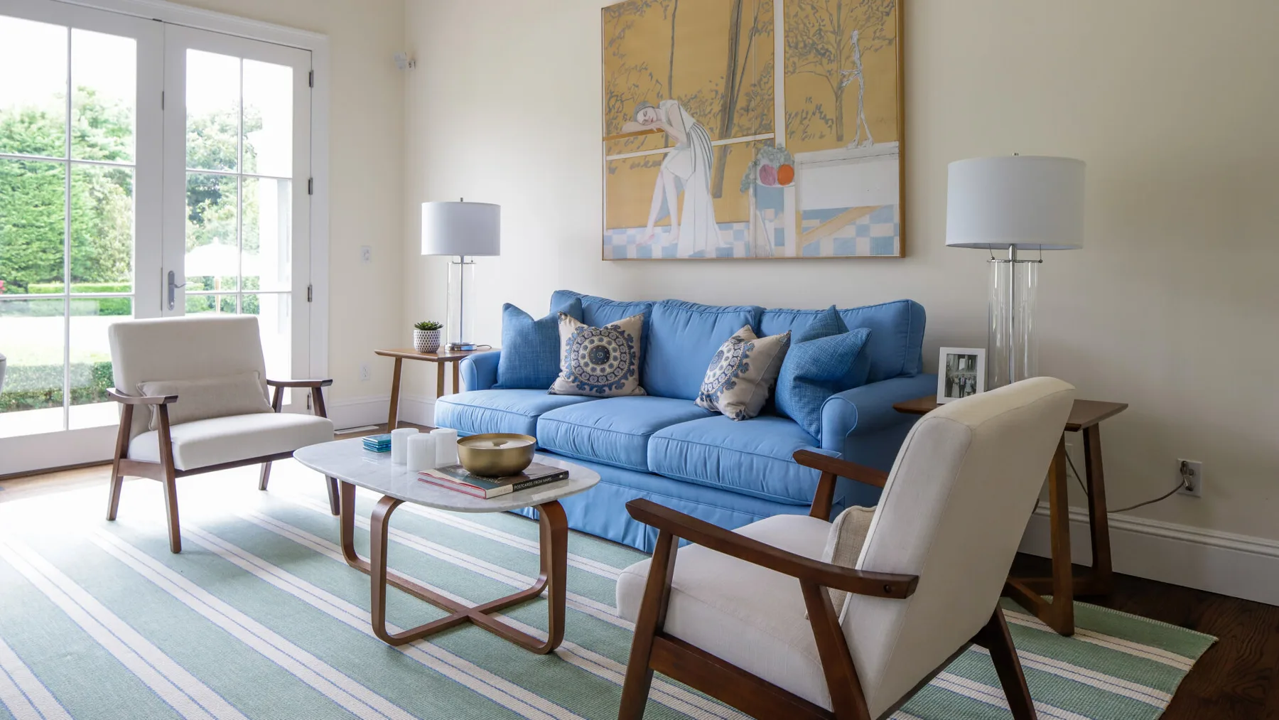 A bright living room with a blue sofa, armchairs, and a striped rug.