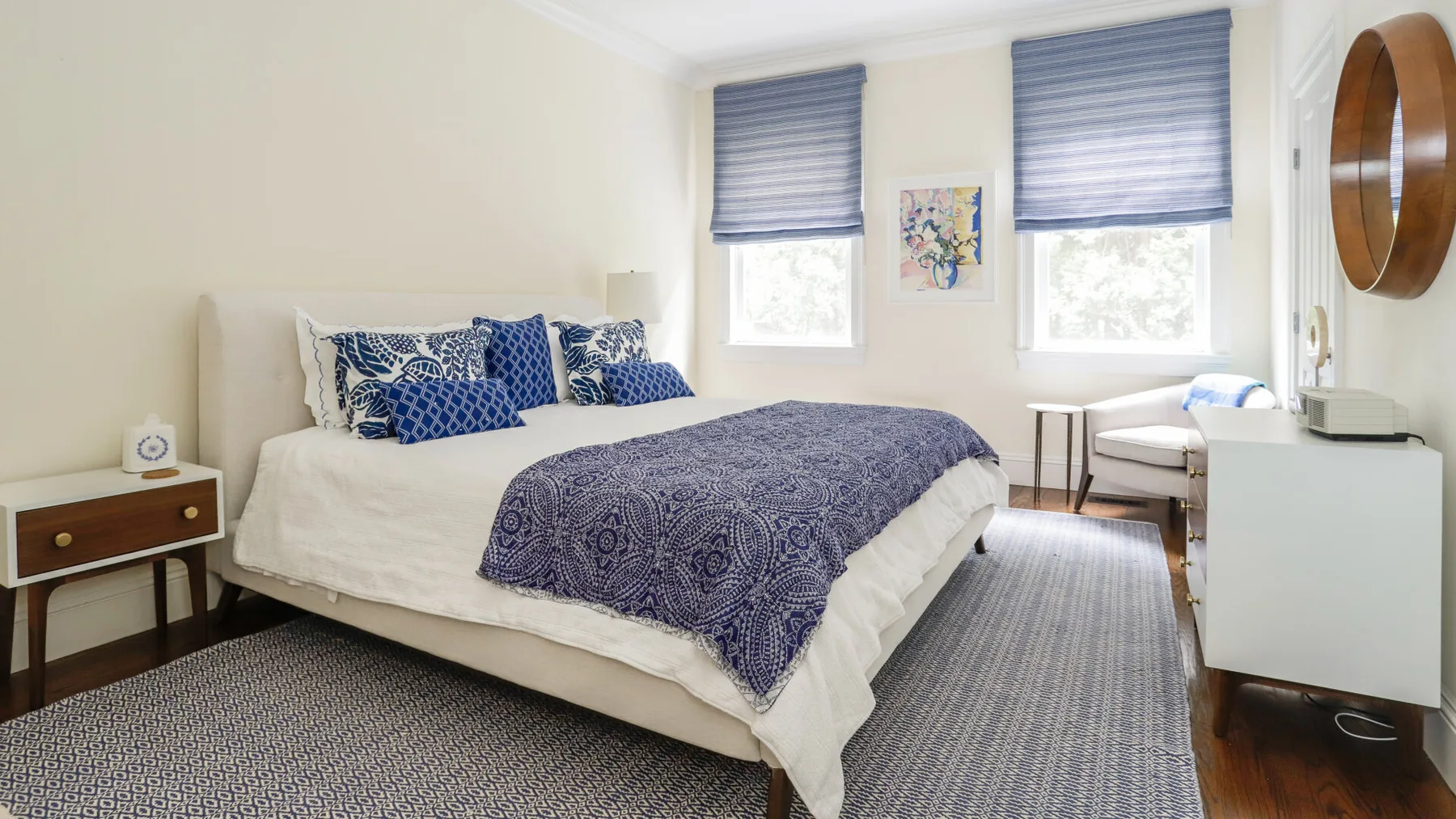 A bedroom with a bed dressed in blue patterned bedding and two windows.