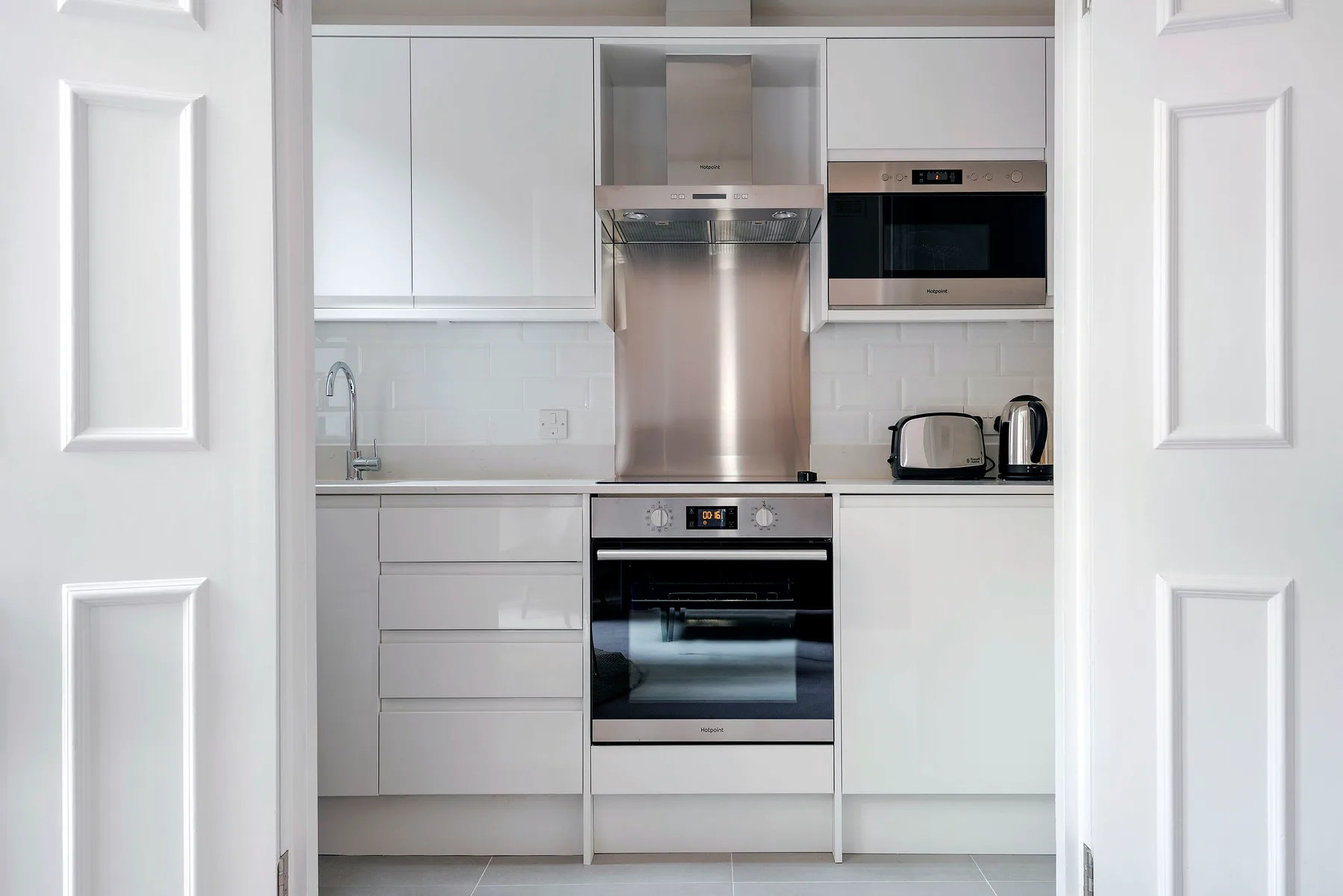 A compact modern kitchen with white cabinets and stainless steel appliances.