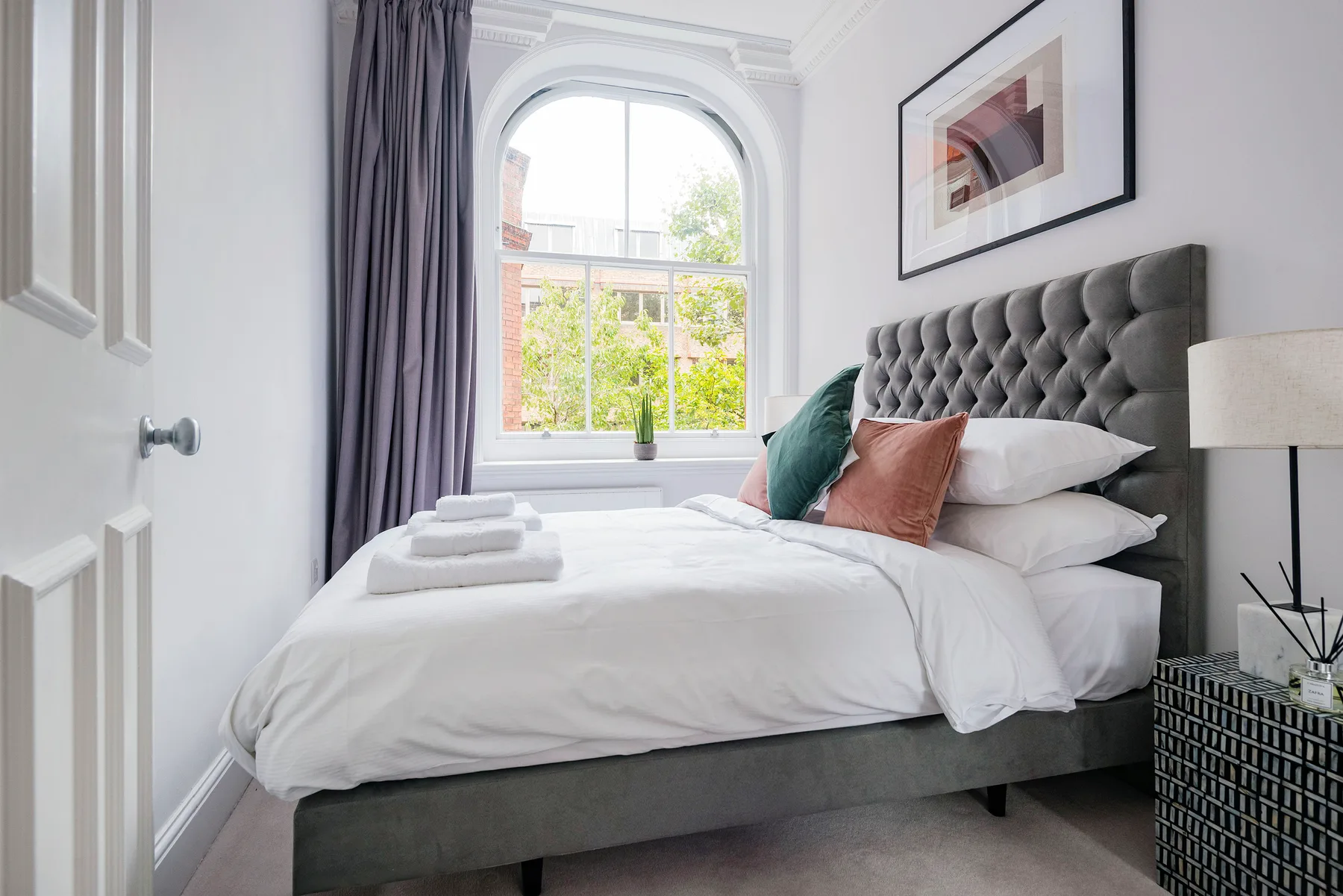 A bright bedroom with a neatly made bed and an arched window.