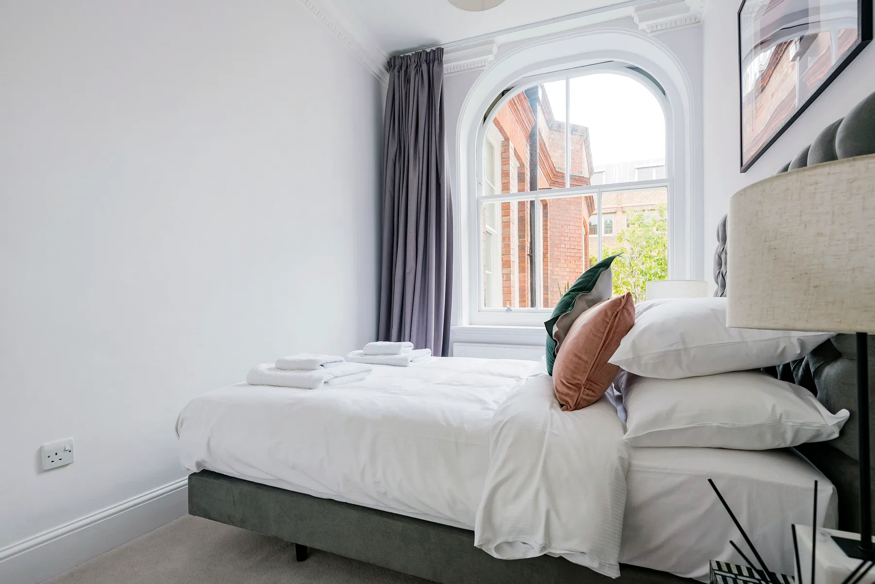 A bright bedroom with white bedding and a large arched window.