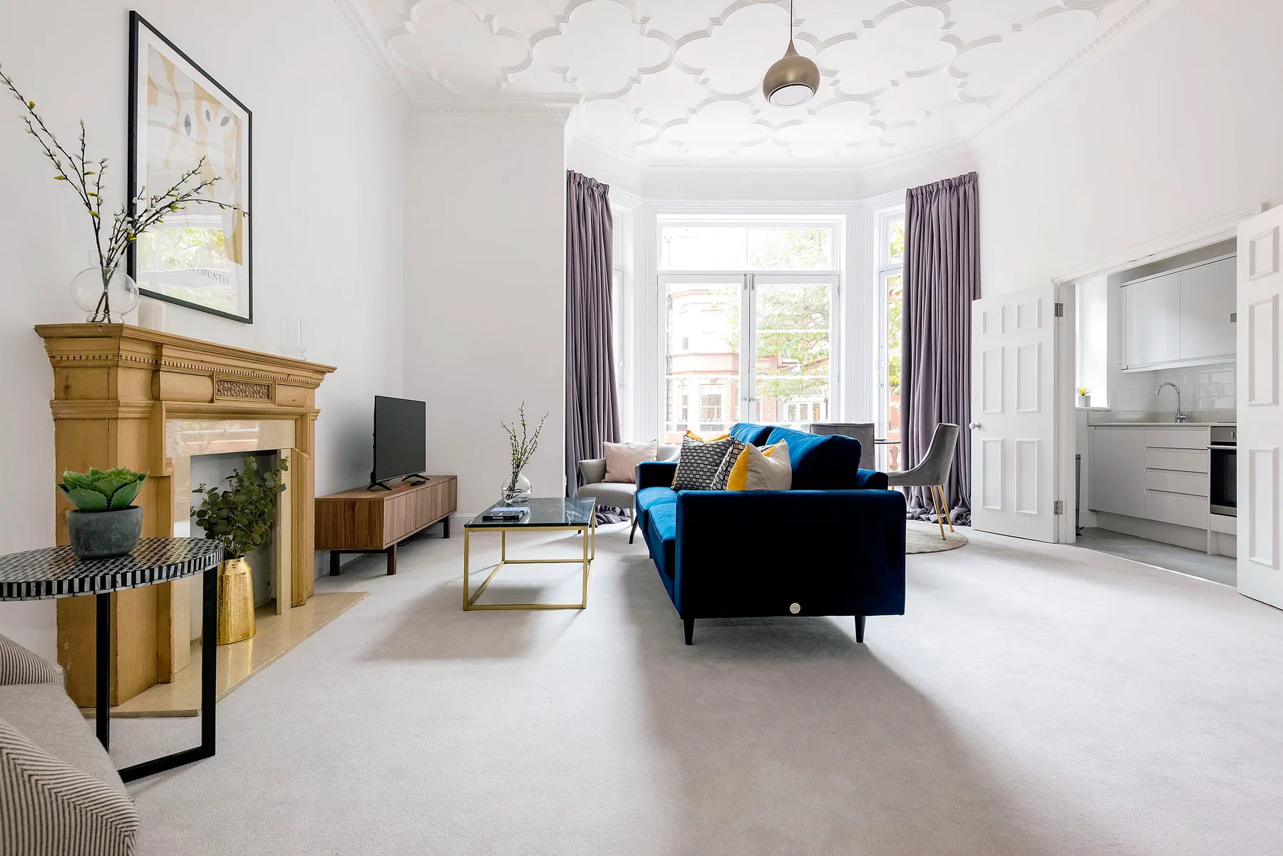 A bright living room with blue seating, a fireplace, and tall windows.