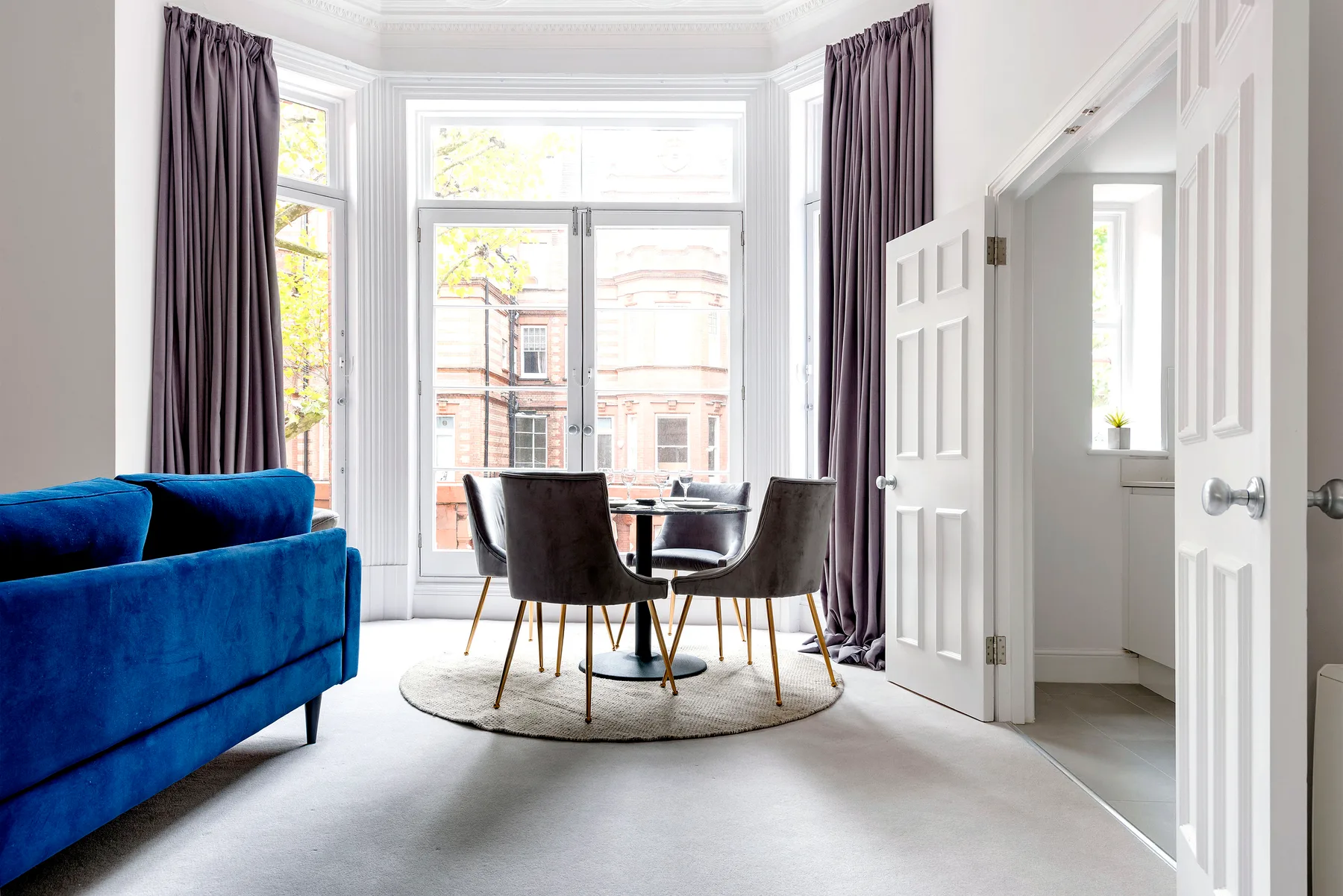 A bright living and dining area with blue seating, a round table, and large windows.