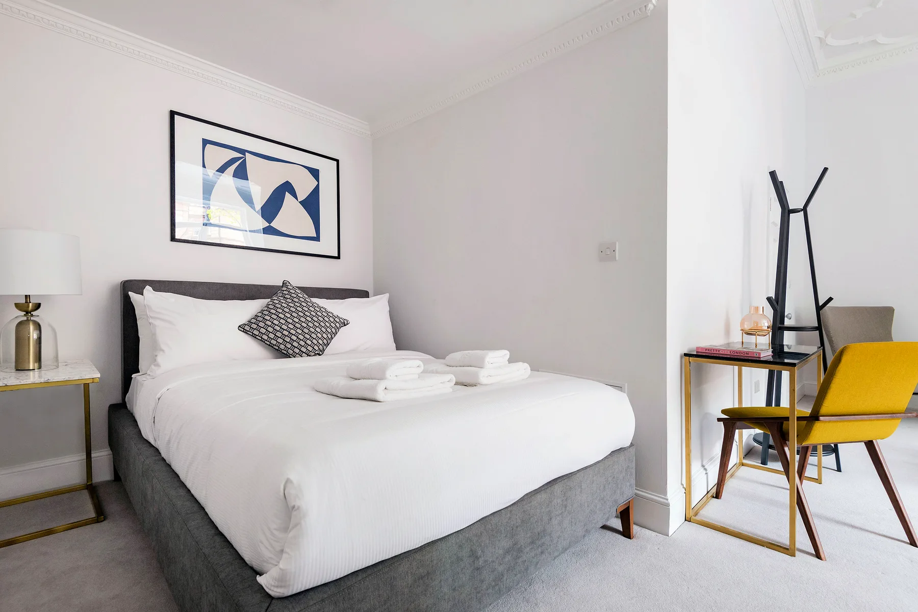 A bright bedroom with a neatly made bed and framed artwork above it.