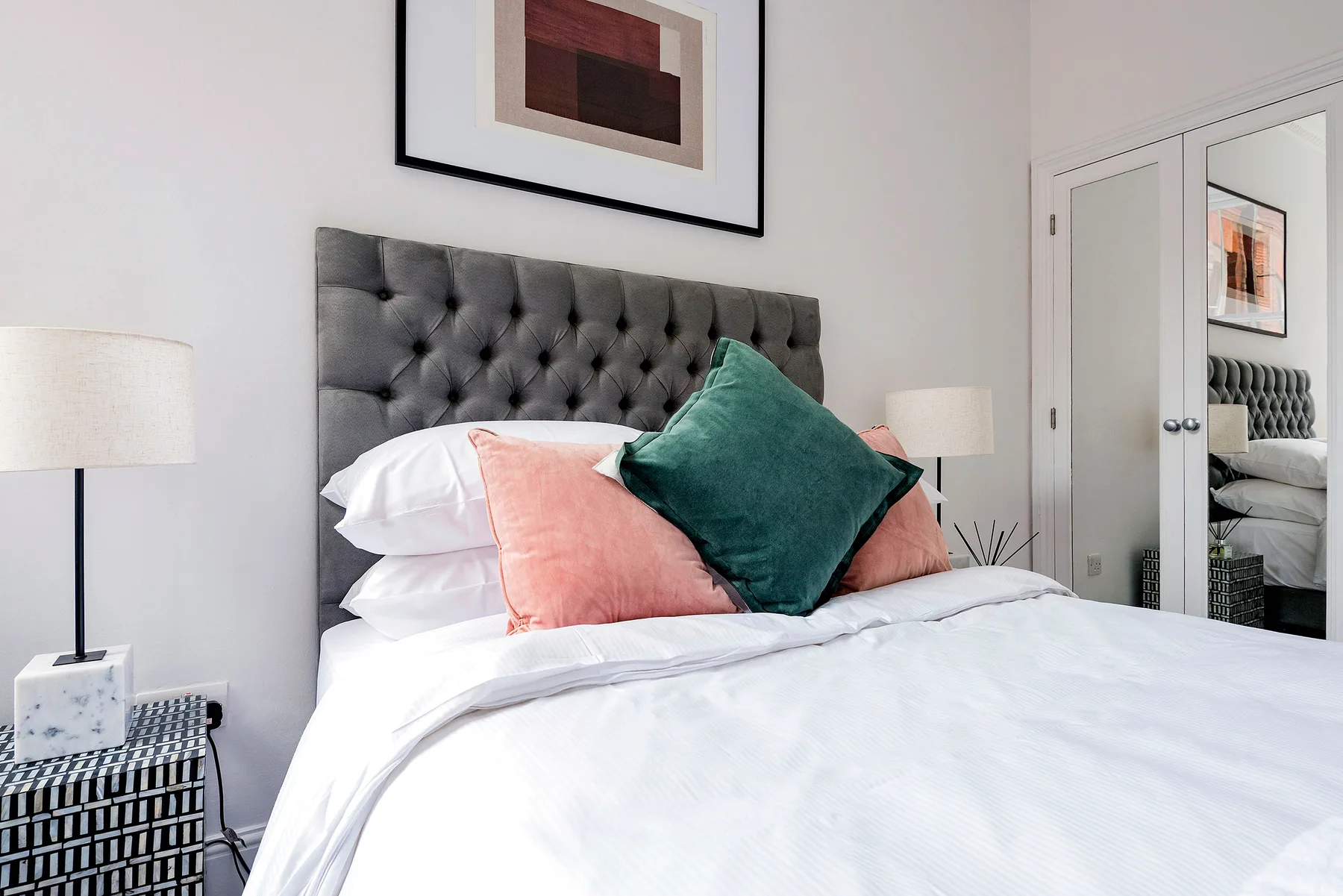 A bedroom with a neatly made bed, colorful pillows, and a tufted headboard.