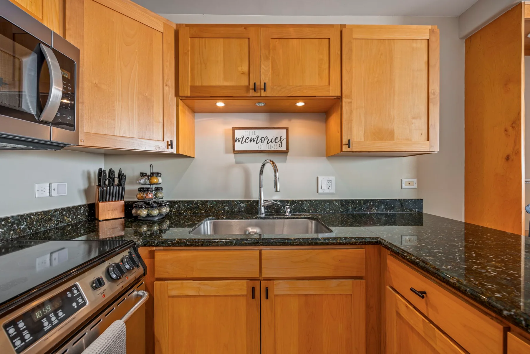 A kitchen with wooden cabinets, dark countertops, and a sink.