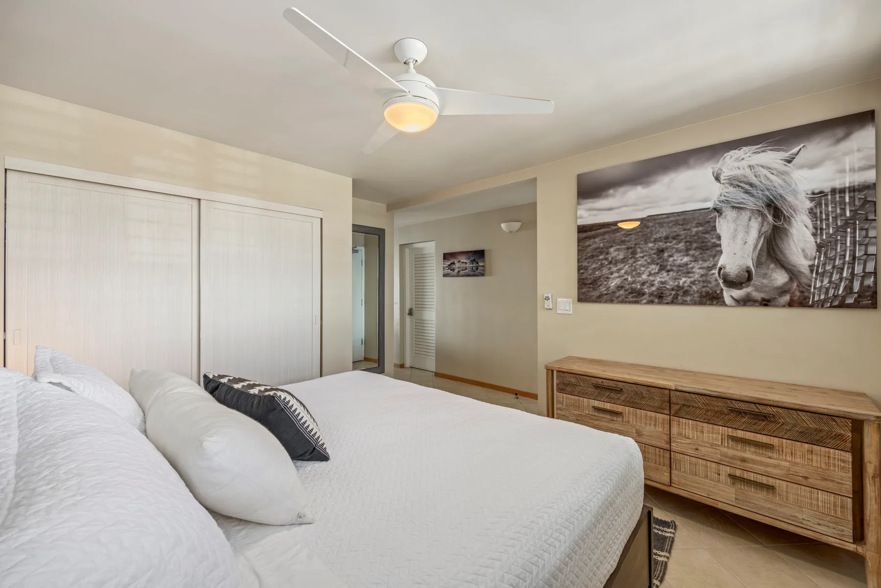 A bedroom with a large bed, closet doors, and a dresser beneath wall art.