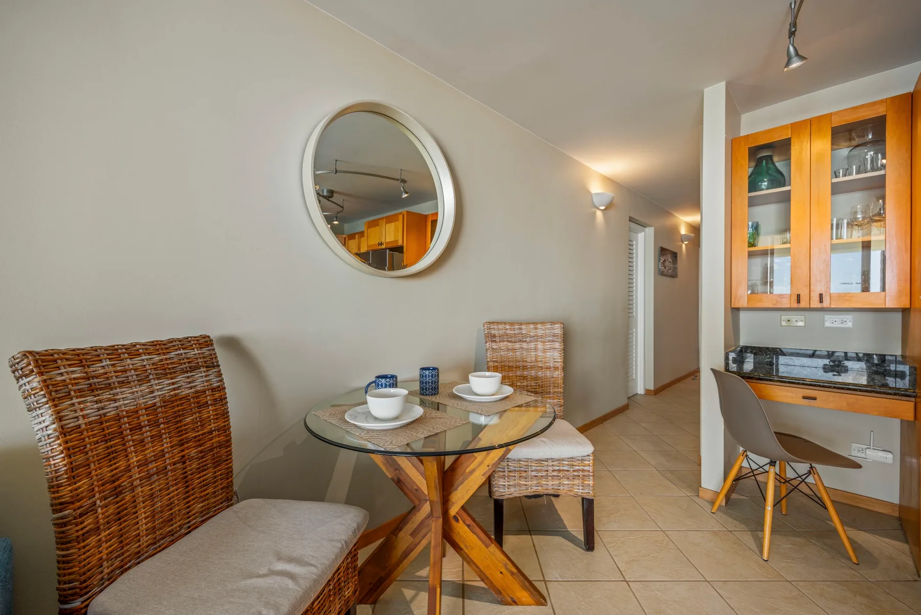 Dining area with a glass table and woven seating beside a wooden cabinet.