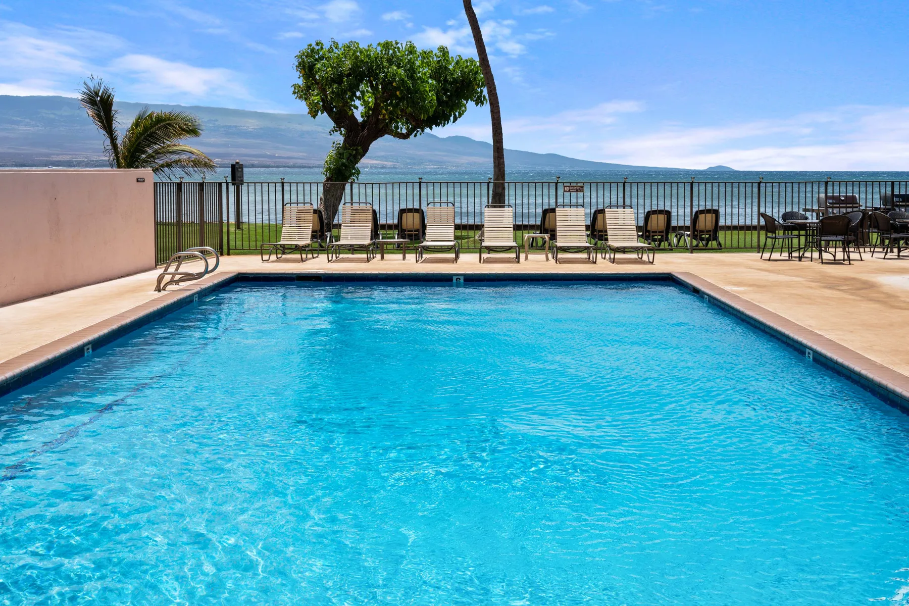 A swimming pool with lounge seating beside a waterfront view.