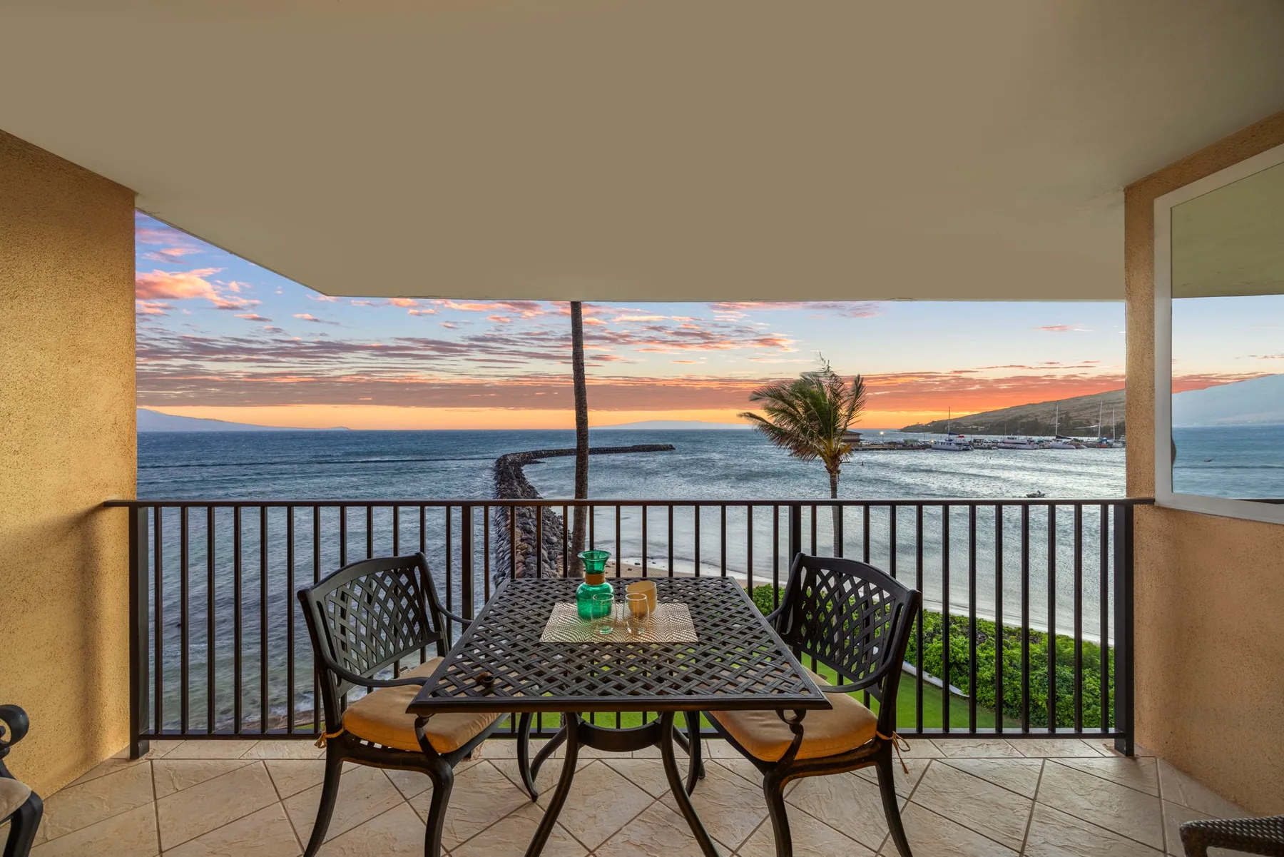 A balcony dining area overlooks the ocean at sunset.