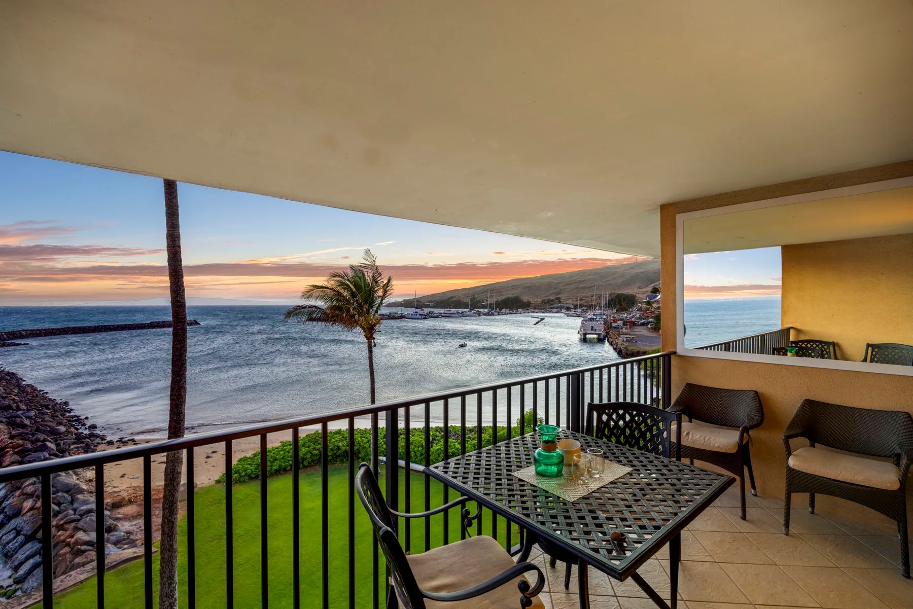 A covered balcony overlooks the water, with a table and seating in the foreground.