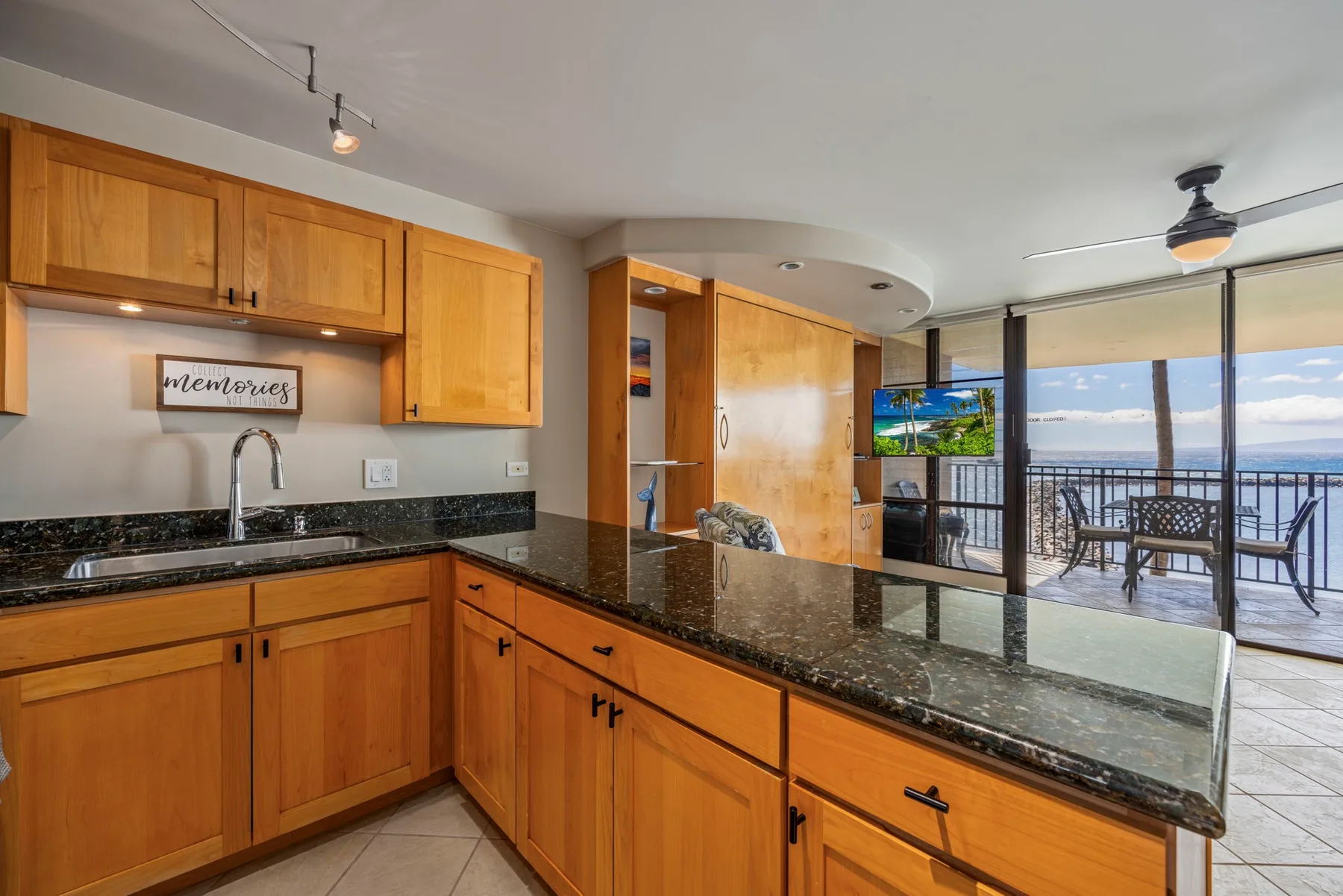 A kitchen with wooden cabinets and a dark countertop opens onto a dining area.