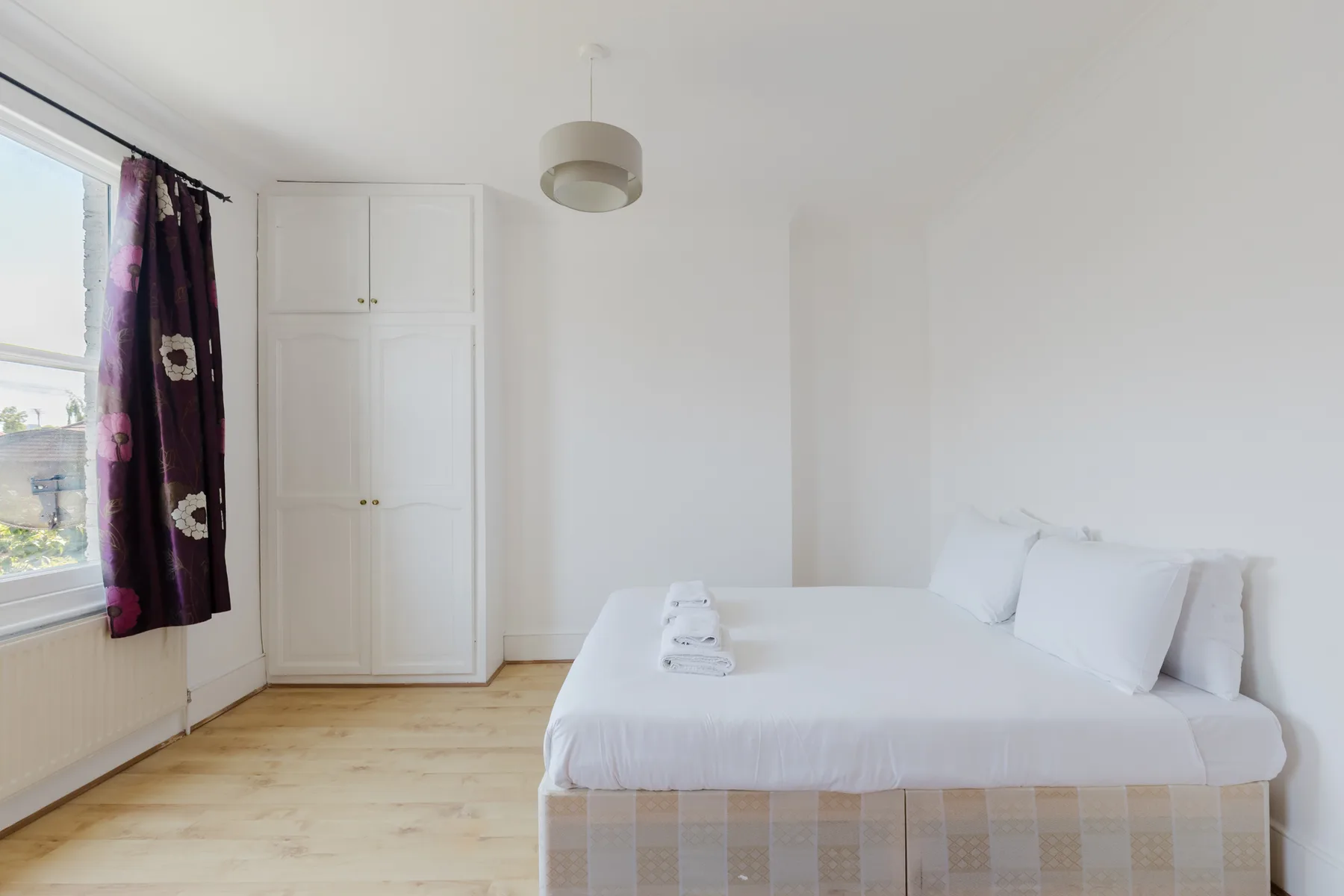 A bright bedroom with a neatly made bed beside a window.