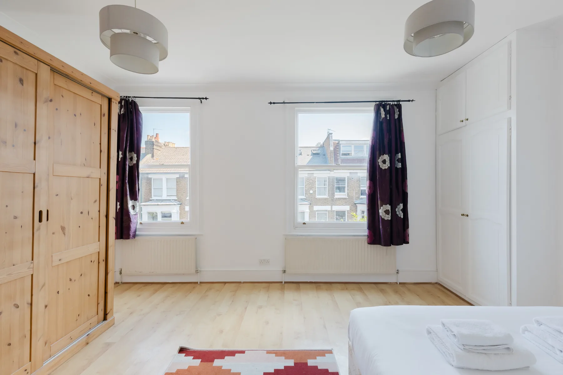 A bright bedroom with two windows, wooden flooring, and a bed.