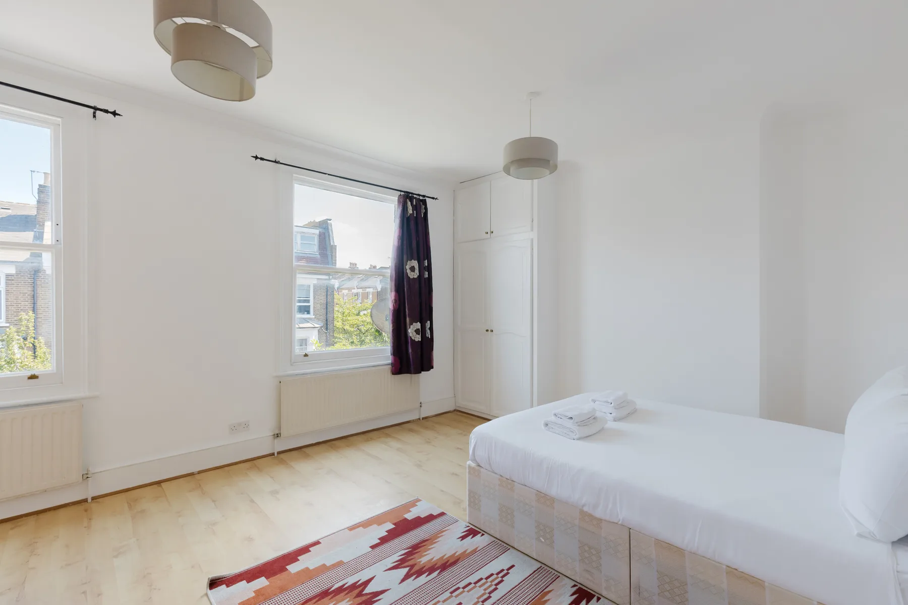 A bright bedroom with a bed, two windows, and a colorful rug.
