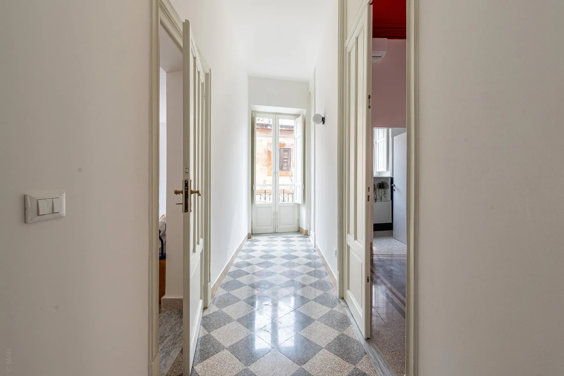 A bright hallway with patterned tile flooring and a window at the far end.