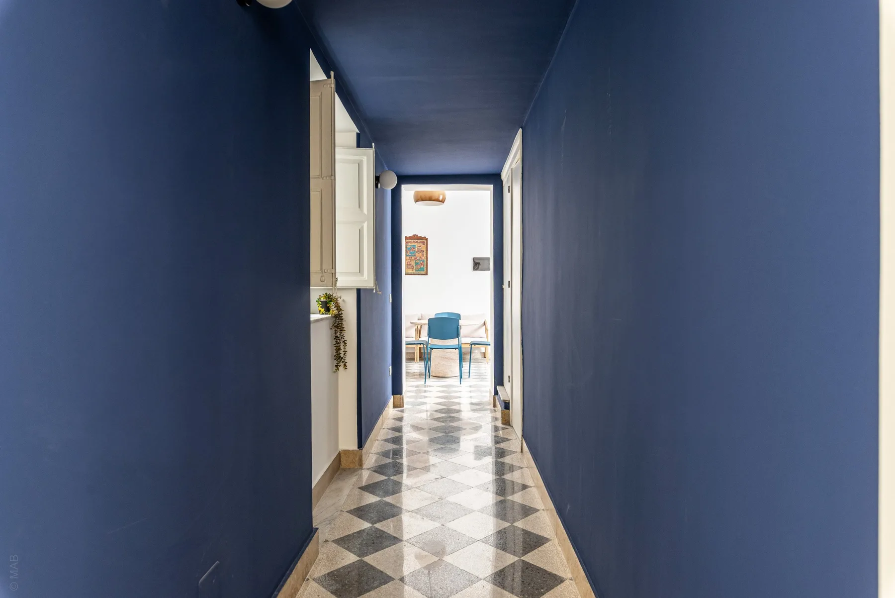 A blue hallway with patterned tile flooring leads to a small dining area.