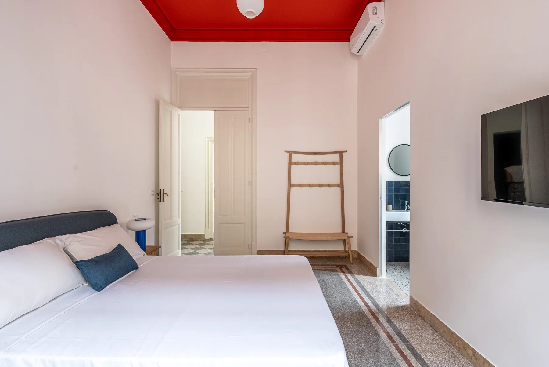 A bedroom with a bed, a wall-mounted television, and a doorway to another room.