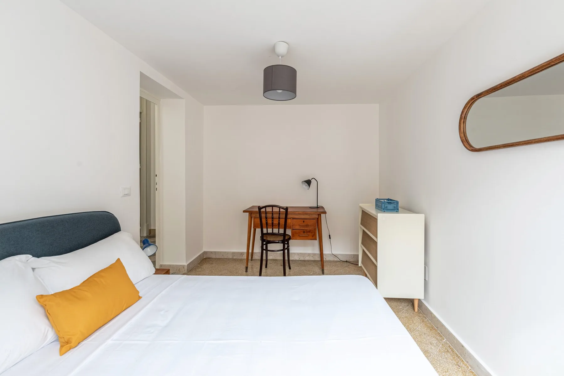 A bedroom with a neatly made bed, a desk, and a chair.