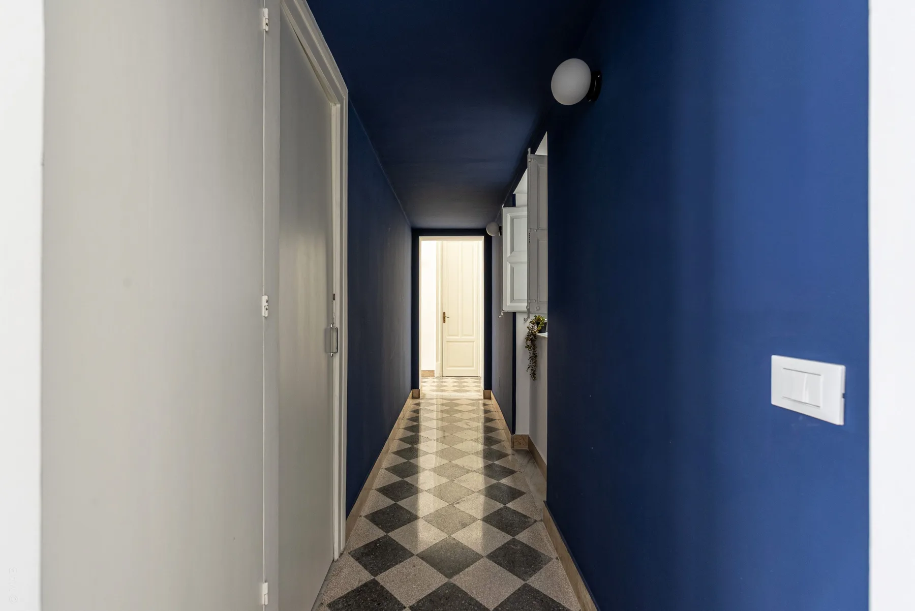 A narrow hallway with dark blue walls and a geometric tiled floor.